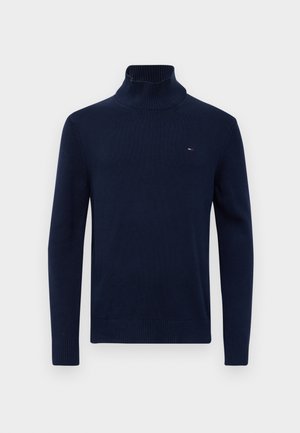 Marineblå ribbad turtlenecktröja med långa ärmar och liten röd, vit och blå logotyp på vänster bröst.