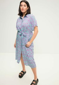 Vestito a maniche corte con un motivo astratto blu e viola, caratterizzato da un colletto, una cintura in vita e uno spacco frontale. Indossato con sandali neri chunky.