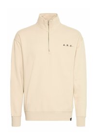 Beige rits-sweater met een hoge kraag, zwarte "A.R.C." letters op de linkerkant van de borst, geribbelde manchetten en een relaxed fit. Zachte stoftextuur.