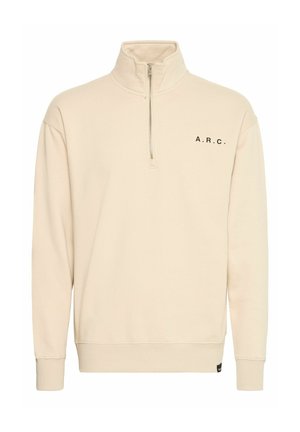 Beżowa bluzka z zamkiem na wysokości szyi, z wysokim kołnierzem, czarnym napisem "A.R.C." na lewej piersi, wzmacnianymi mankietami i luźnym krojem. Miękka faktura materiału.