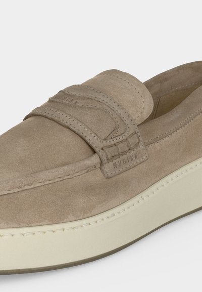 Mocassin beige en daim avec des détails cousus, une bride sur le dessus et une semelle épaisse en caoutchouc blanc cassé.