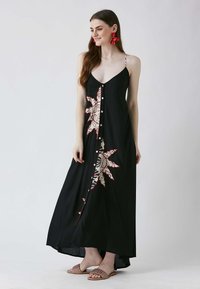 Svart maxiklänning med spaghettiband, har ett blommönster i röd och kräm, knappstängning fram och en flödande silhuett.
