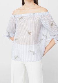 Schulterfreies, durchscheinendes Blusenshirt in Hellblau mit weißen Streifen, verziert mit silberner Vogelstickerei und kurzen, gebundenen Ärmeln.