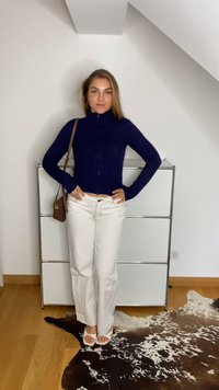 Mörkblå ribbad sweater med hög halsringning, i kombination med vita raka byxor och vita sandaler. Minimalistisk brun axelremsväska som accent.