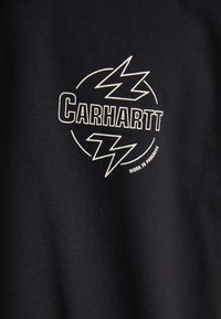 Camiseta de algodón negra con un logotipo gráfico en blanco que presenta motivos de rayos y texto que dice "Carhartt" y "WORK IN PROGRESS."
