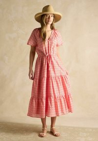 Ružová kvetinová maxi šaty s krátkymi rukávmi, opaskom na viazanie a volánovým lemom. Doplněné širokým slamenným klobúkom a sandálmi.