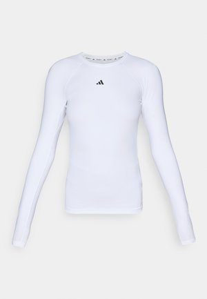 Dlouhý rukáv bílého sportovního trička vyrobeného z elastické tkaniny, s kulatým výstřihem a malým černým logem na oblasti hrudi.
