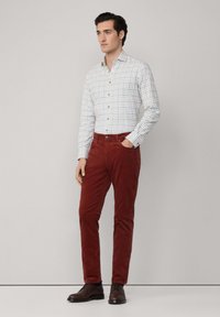 Weißes karierter Hemd mit blauen und grünen Linien, kombiniert mit tiefroten Kordhosen und braunen Dressschuhen.