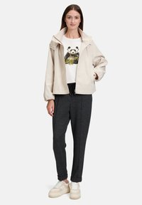 Jasnobeżowa kurtka z wysokim kołnierzem, zestawiona z białym t-shirtem z grafiką pandy oraz ciemnoszarymi, zwężanymi joggerami. Białe trampki.