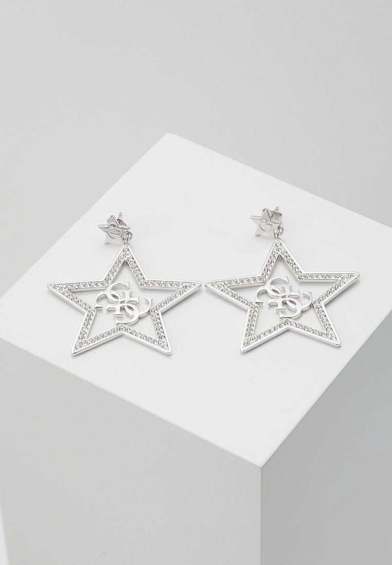 Boucles d'oreilles pendantes en forme d'étoile en argent, avec de petits cristaux bordant les étoiles et des lettres décoratives entrelacées à l'intérieur.