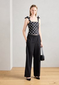 Black polka dot crop top with square neckline and bow straps, paired with high-waisted black trousers and black heels. Small black handbag.