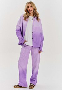 Fialová džínová bunda s gradientovým ombré efektem, spárovaná s odpovídajícími fialovými kalhotami. Dokončeno bílým topem a teniskami s leopardím vzorem.