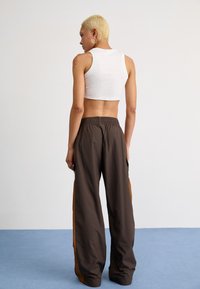 White cropped tank top paired with loose-fitting brown pants featuring orange side panels and an elastic waistband. Smooth texture throughout.