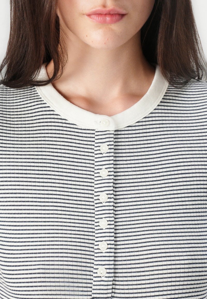 Bluzka w paski z poziomymi liniami w kolorze granatowym i białym, z beżowym, prążkowanym kołnierzykiem i listwą z sześcioma guzikami. Miękka faktura.