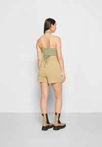 Top cropped verde com alças, feito de um tecido texturizado, combinado com calções beiges e botas de tornozelo grossas em tom de castanho. O conjunto exibe um estilo casual.