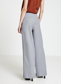 Hellgraue Weitbein-Hose aus strukturiertem Stoff mit hoher Taille und dezenten Gesäßtaschen, kombiniert mit schwarzen Absätzen.