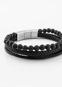 Black braided leather bracelet featuring textured lava stone beads and a metallic clasp with a lotus design. Durable and versatile accessory.