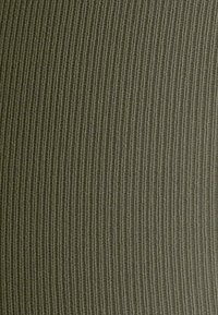 Tessuto a coste di un verde oliva tenue, con una superficie testurizzata caratterizzata da linee verticali. Materiale morbido e elastico, vista ravvicinata.