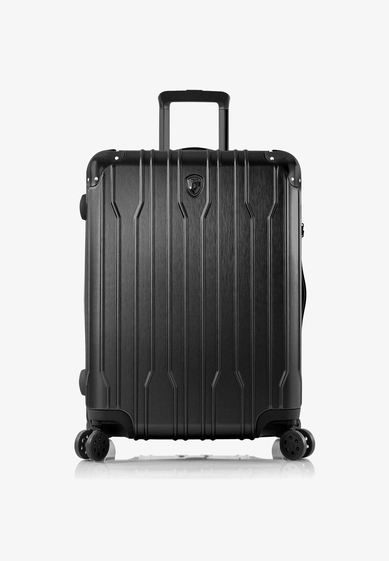 Schwarzer Hartschalenkoffer mit vertikalen Rillen, teleskopischem Griff, vier drehbaren Rollen und einem Logoemblem an der Oberseite. Glatte Textur.