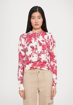Cardigan leggero a maglia con motivo floreale rosso, caratterizzato da un design cropped, scollo rotondo e chiusura con bottoni. Abbinato a pantaloni beige.