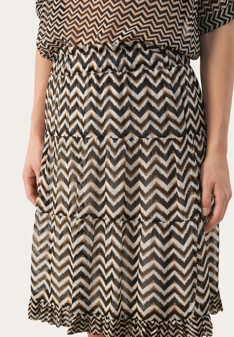 Jupe transparente à motifs zigzag noire, blanche et brune avec un ourlet à volants, une taille élastique et un design à étages. Matière légère.