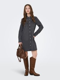 Donkergrijze denim jurk met knoopsluiting aan de voorkant, twee borstzakken en lange mouwen. Gecombineerd met bruine leren cowboylaarzen en een handtas.