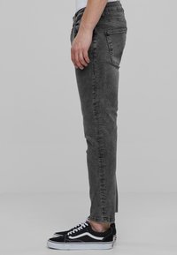 Jeans de mezclilla gris con un corte ajustado, que presentan una cintura de altura media, bolsillos traseros y un acabado desgastado, complementados por zapatillas negras con suelas blancas.