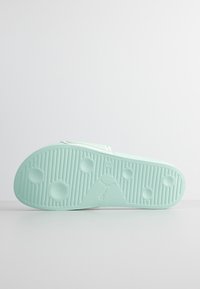 Semelle de sandale en caoutchouc vert menthe avec des rainures texturées, des motifs hexagonaux et un logo central, conçue pour l'adhérence et le confort.