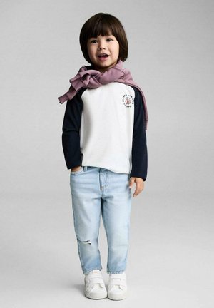 Vit och marinin blå långärmad tröja med logotyp, ljusblå slitna jeans och vita sneakers; en inlindad rosa scarf ger extra detalj.