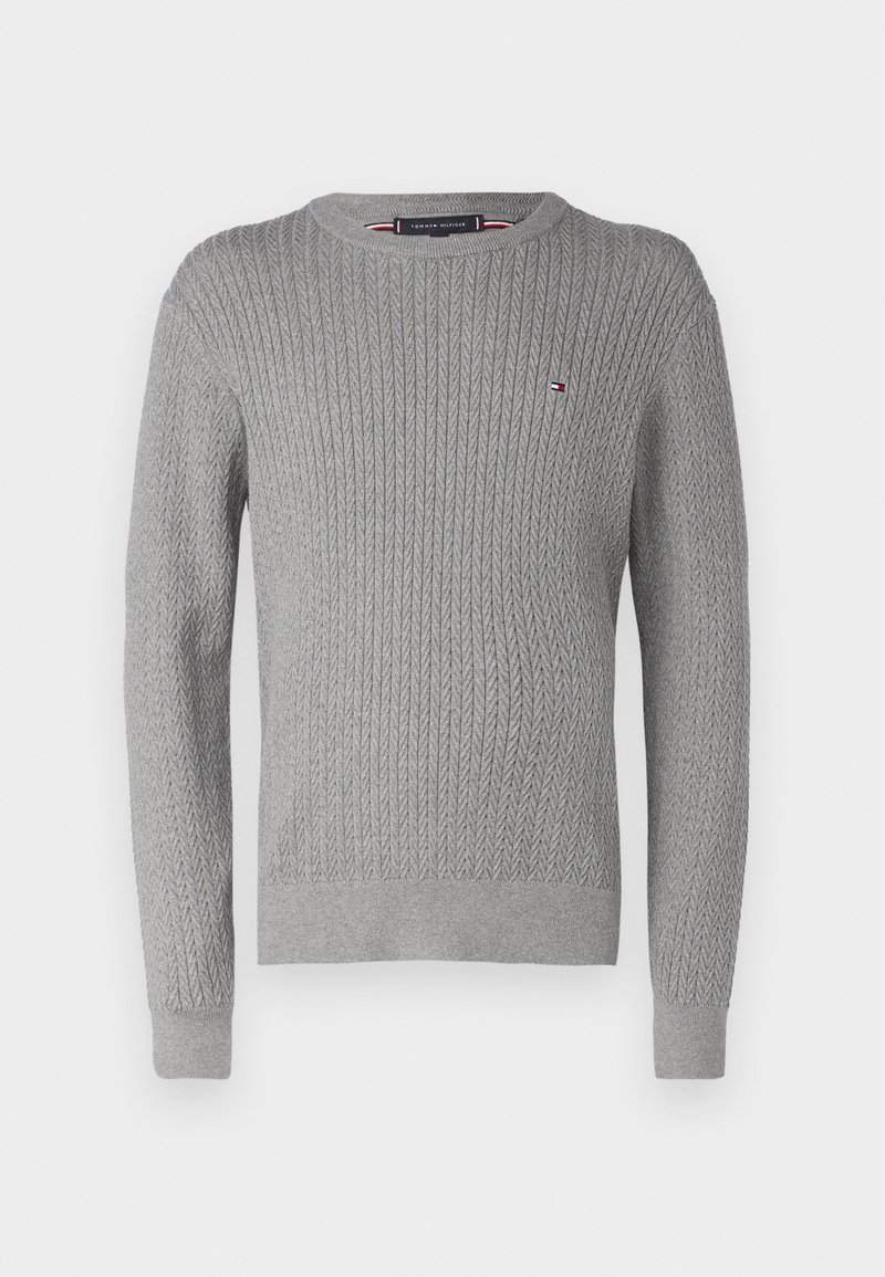 Pull en tricot gris à col rond, manches longues et poignets et ourlet côtelés. Présente un petit logo sur la poitrine gauche.