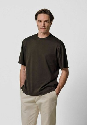 T-shirt a maniche corte di colore marrone scuro con collo rotondo, realizzata in tessuto morbido, abbinata a pantaloni beige chiaro. Design minimalista, senza motivi.