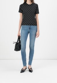 Černé tričko s puntíky a krátkým rukávem, doplněné světle modrými skinny džíny. Černá kabelka a špičaté slingback boty dotvářejí celkový vzhled.