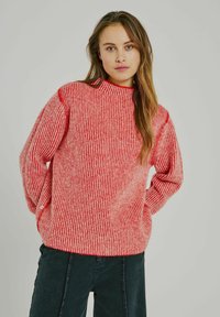 Maglione a righe rosse e beige con collo alto, vestibilità oversize, texture a coste e spalle scese, abbinato a jeans neri.