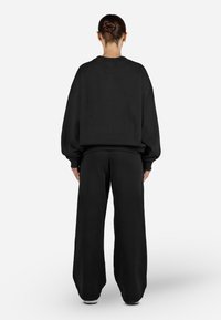 Čierna oversized mikina s poklesnutými ramenami, spárovaná s širokými čiernymi teplákmi. Mäkká textúra, minimalistický dizajn, bez viditeľných log alebo vzorov.
