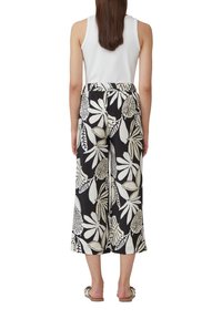 Pantalons larges en tissu noir avec un motif de feuilles blanches. Taille élastique, coupe décontractée et longueur courte. Associés à un débardeur blanc.