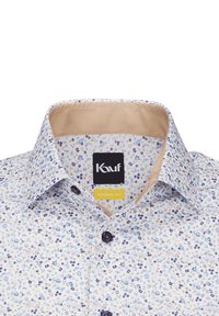 Blumenhemd mit weißem Hintergrund, das blaue, lila und braune Blumen zeigt. Mit Kragen, einem beigen Innenfutter und dunklen Knöpfen.
