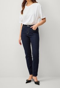 Ciemnoniebieskie skinny jeans z wysokim stanem, z jasnym przeszyciem i pięcioma kieszeniami. Noszone z luźnym białym t-shirtem i czarnymi szpilkami.