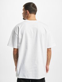 Valge suur oversized T-särk, mis on valmistatud puuvillast, lühikeste varrukatega ja ümmarguse kaelusega, nähtud tagantpoolt lihtsa tekstuuriga.