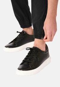 Sneaker nere in pelle con una superficie liscia, suola in gomma bianca e design classico con lacci. Presentano perforazioni per una migliore traspirabilità.