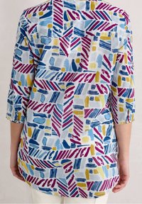 Top ligero y estampado con diseños de pinceladas en azul, púrpura y amarillo sobre un fondo blanco, con mangas tres cuartos y dobladillo redondo.