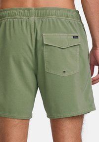 Shorts de bain verts avec une taille élastique, poche arrière avec rabat et détail d'œillet en métal, fabriqués en tissu lisse et léger.