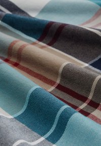 Gewebter Stoff mit einem Fischgrätmuster, das blaue, beige, rote und graue Streifen aufweist. Strukturierte Oberfläche mit abwechselnden Farbbereichen.