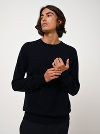 Dunkelblauer Wollpullover, runder Halsausschnitt, lange Ärmel, gerippte Bündchen und Saum, weiche Textur, taillierte Passform, getragen von einem Modell mit hellen Locken.
