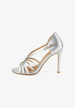Ezüst magas sarkú szandál nyitott orral, több vékony pánttal és állítható bokapánttal, fehér háttér előtt.