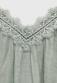 Tessuto in lino verde chiaro con un intricato bordo in pizzo sul colletto, caratterizzato da un motivo a onde e delicati accenti ricamati.
