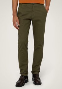 Olivgröna bomullschinos i slim fit, med knappstängning, sidofickor och synliga sömmar. Bärs med svarta loafers.