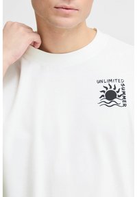 Hvid bomuld t-shirt med et brystgrafik, der har teksten "UNLIMITED SUMMER" samt et sol- og bølge-design i sort. Rund hals design.