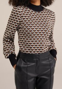 Stickad tröja i brunt, krämfärgat och svart geometriskt mönster, med ribbad svart halsringning och ärmar. Matchad med svarta läderbyxor.