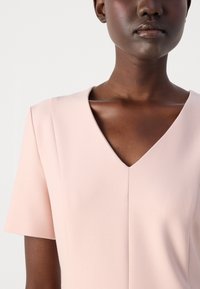 Soft pink dress featuring a V-neckline and short sleeves. The smooth fabric has a subtle texture with neat seams and a fitted silhouette.