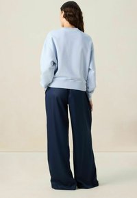Lichtblauwe sweatshirt met verlaagde schouders en geribde zoom, gecombineerd met marineblauwe wijde broek, beide gemaakt van zachte stof.